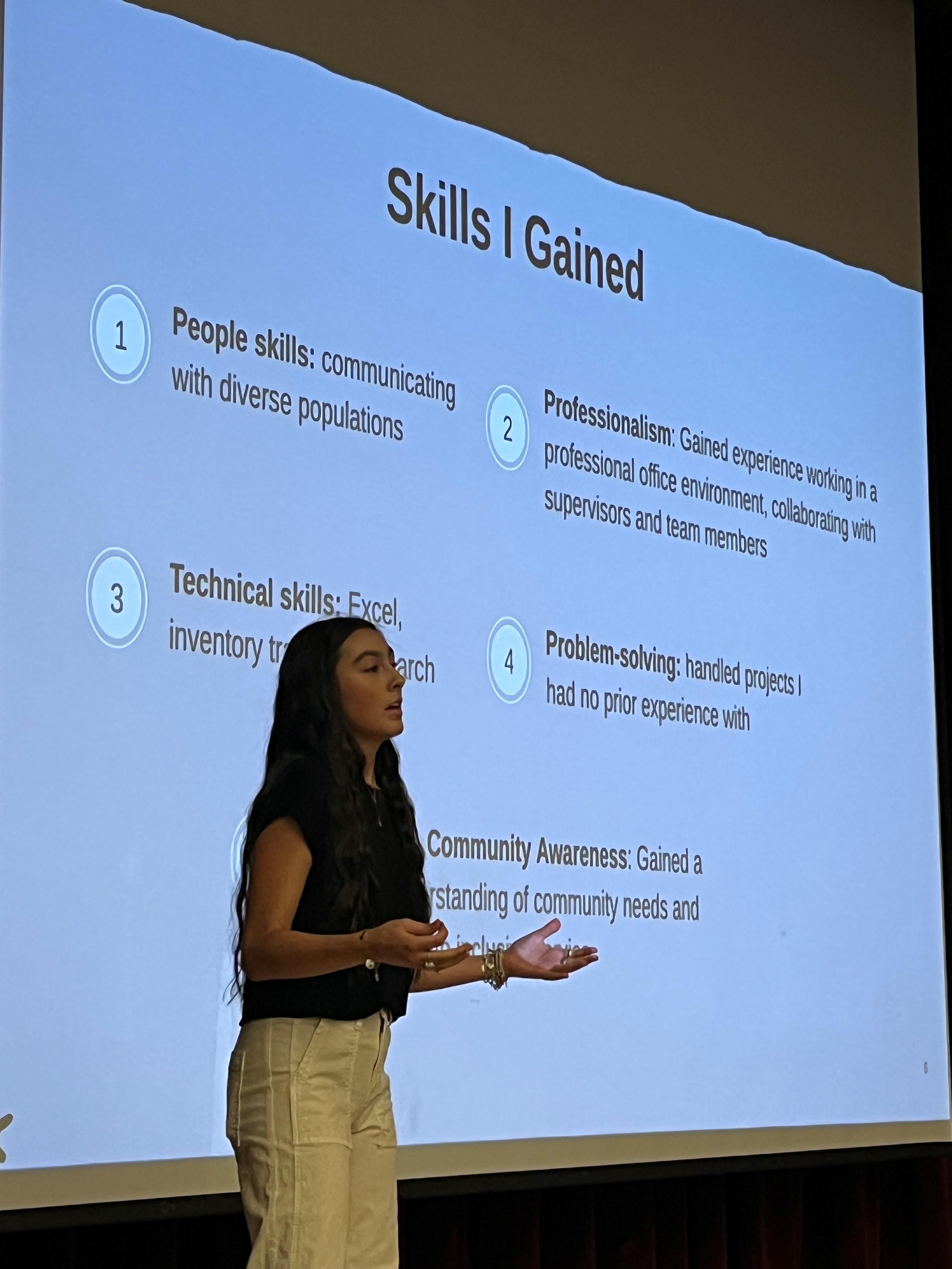 intern presenting about her lessons learned, on a stage in front of a projection of her slides